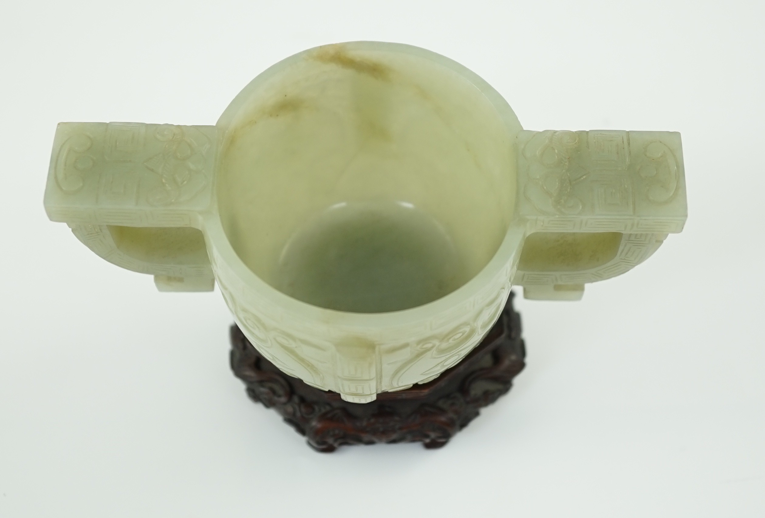 A Chinese archaistic celadon jade two handled cup, 17th century, 12.9cm across 6.1cm high, associated wood stand